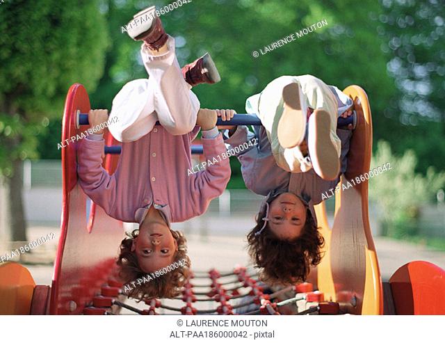 Two children hanging upside down on jungle gym