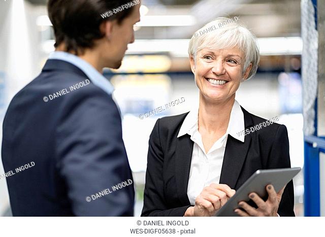 Smiling businessman and senior businesswoman with tablet talking in a factory