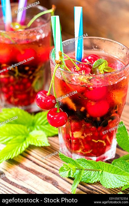 Glasses of refreshing drink flavored with fresh fruit and decorated with cherries covered with dew drops. Wooden background