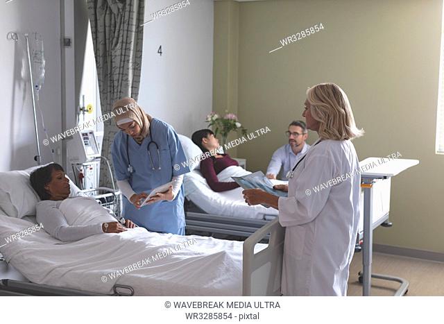 Side view of diverse female doctors showing medical report to mixed-race female patient on digital tablet in the ward at hospital