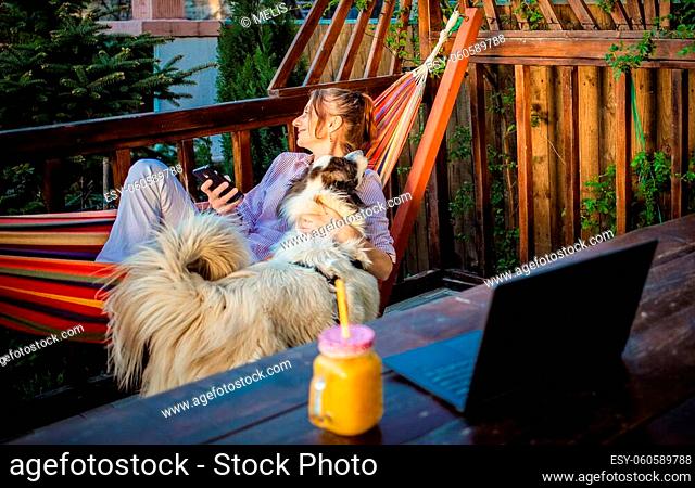 woman with laptop and white shepherd dog in a hammock in backyard summer home office