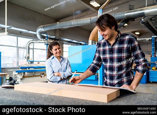 Manual worker measuring wood while standing by colleague at industry