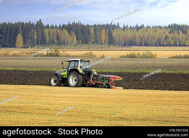 Farmer plows field with green Valtra tractor and plough on a sunny autumn morning in South of Finland. Jokioinen, Finland. October 2, 2020