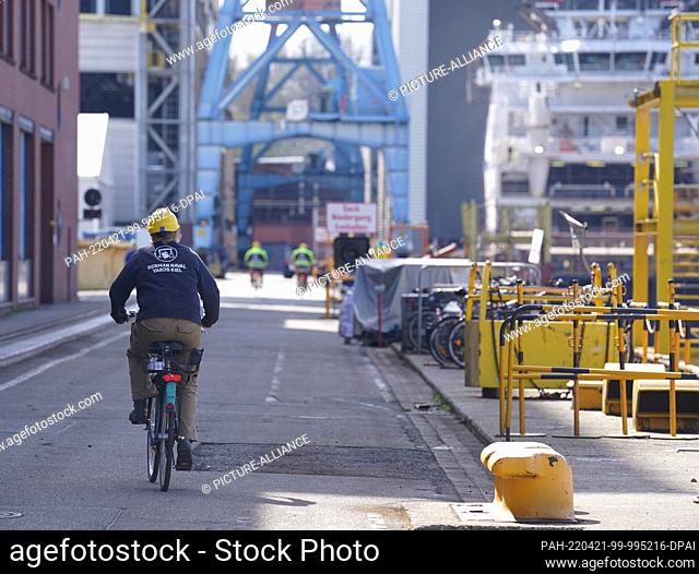 21 April 2022, Schleswig-Holstein, Kiel: Shipyard workers ride a bicycle across the grounds of the German Naval Yards shipyard