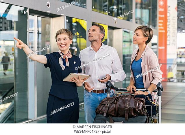 Airline employee assisting couple with baggage cart at the airport