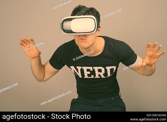 Studio shot of young handsome nerd man wearing virtual reality headset against gray background