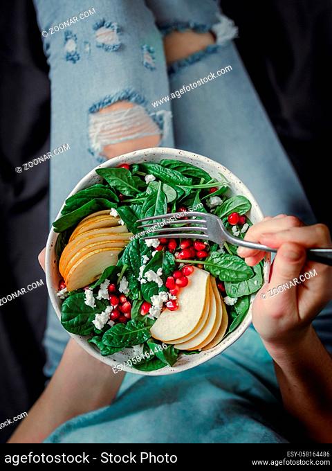 Woman in jeans holding vegan salad bowl with spinach, pear, pomegranate, cheese. Vegan breakfast, vegetarian food, diet concept