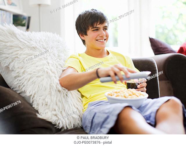 Smiling teenage boy sitting with popcorn and remote control