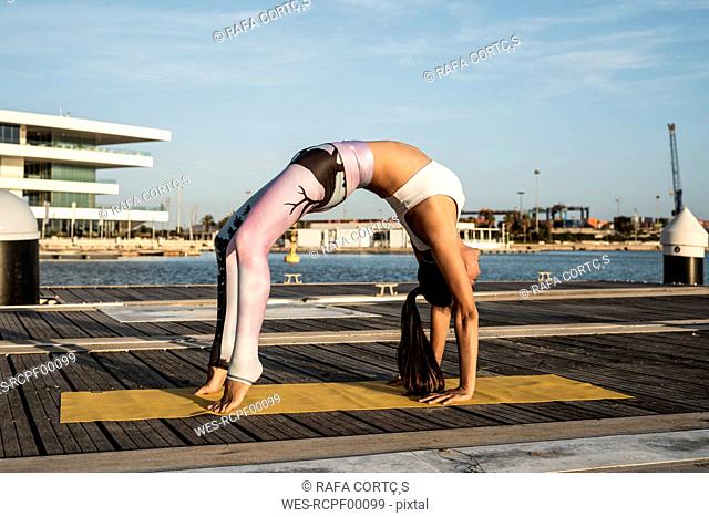 Asian woman practicing yoga on a pier at harbour, upward bow