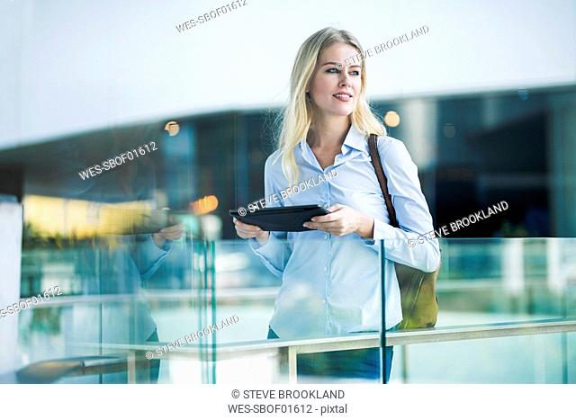 Blond woman with tablet standing at glass railing in the city