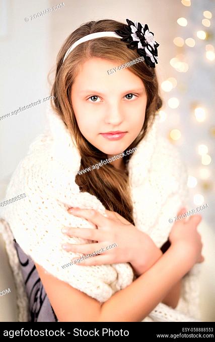 Portrait of a pretty smiling teen girl wrapped in a warm knitted sweater in interior with Christmas decorations