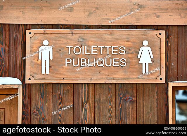 Public toilets signs on a wooden building in France. Sign in French reads Public Toilets translated to English