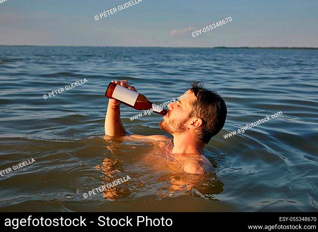 Young man having a good time drinking beer and refreshing in the water at the beach