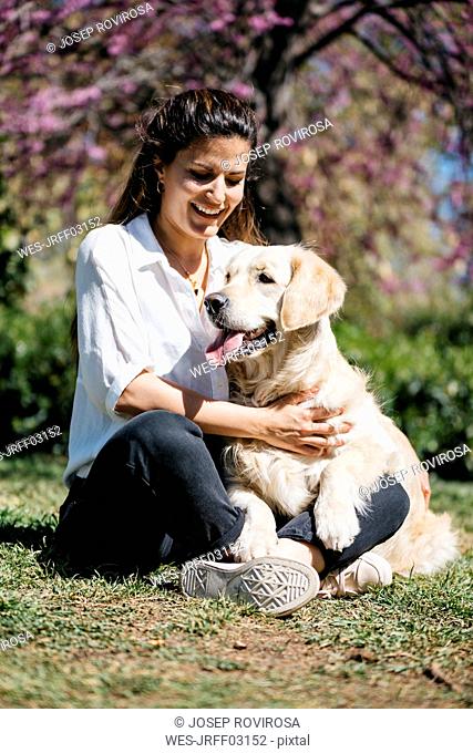 Happy woman sitting on meadow in city park with her Labrador Retriever