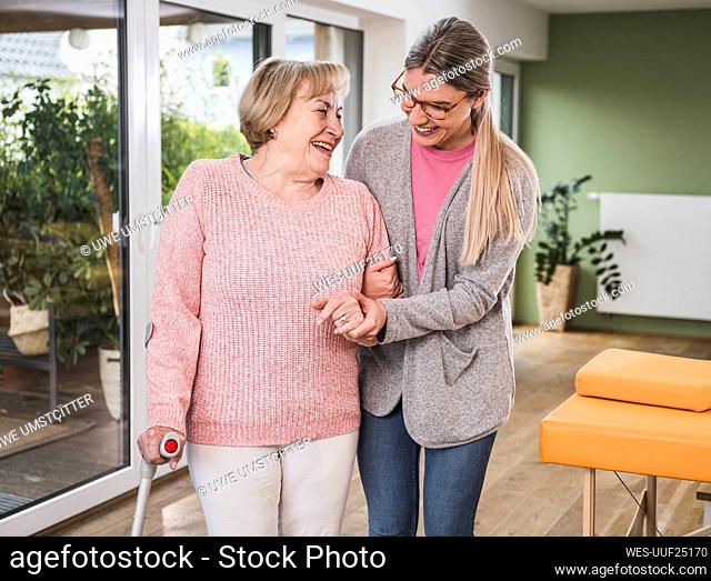 Smiling caregiver helping disabled woman to walk at home