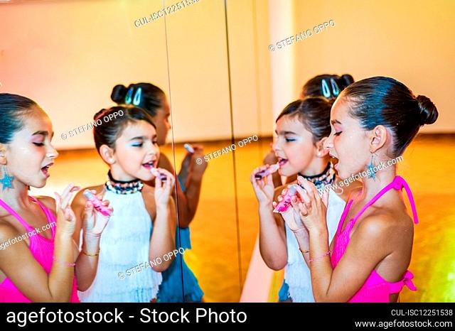 Young girls in dance class, getting ready for a performance, standing in front of mirror, applying lipstick
