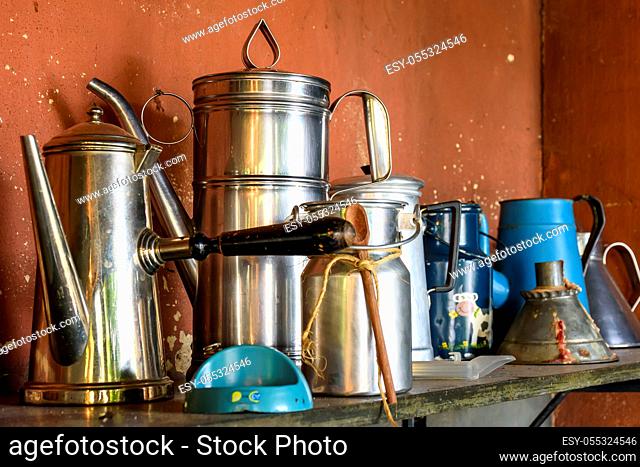 Collection of old and used coffee pots on brazilian farm arranged on wooden shelf with rustic wall behind