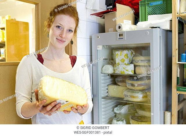 Portrait of smiling young woman in wholefood shop holding piece of cheese