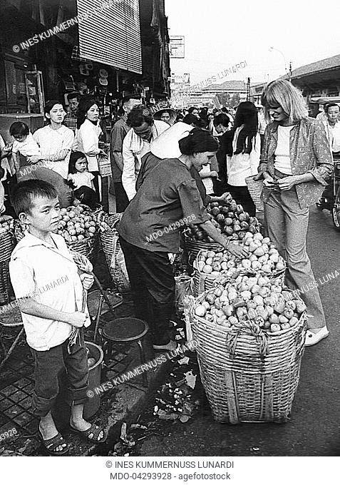 Ines Kummernuss Lunardi - model for the magazine Grazia - buying fruits in the street. Vietnam, 1973