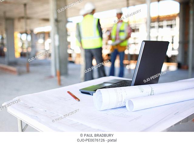 Construction workers behind blueprints and laptop on construction site