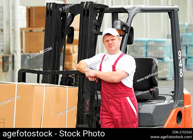 young cheerful warehouse worker driver in uniform in front of forklift stacker loader