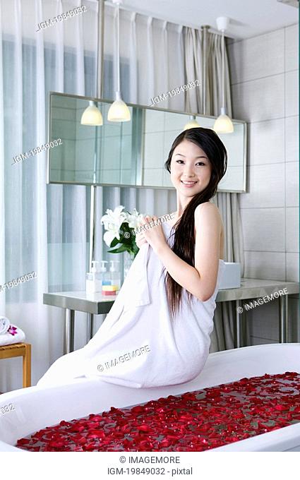 Young woman wearing a towel and sitting on the bathtub