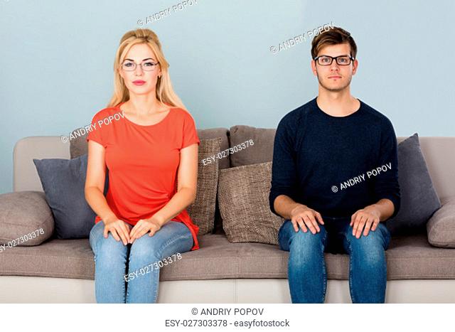 Portrait Of Man And Woman Wearing Glasses Sitting On Couch At Home