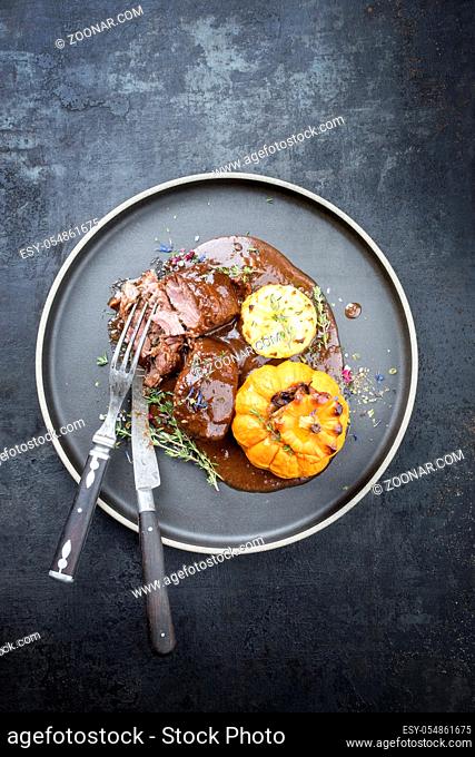 Traditional German braised pork cheeks in brown red wine sauce with fried mushed potatoes and pumpkin as top view on a modern design plate with copy space