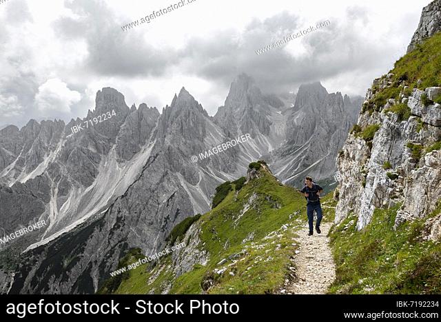 Hikers on a trail, mountain peaks and pointed rocks in the background, dramatic cloudy sky, Cimon di Croda Liscia and Cadini group, Auronzo di Cadore, Belluno