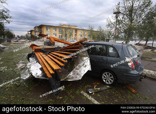26 August 2023, Bavaria, Kissing: A roof of a senior citizen's home removed by the storm lies on top of a car in a parking lot