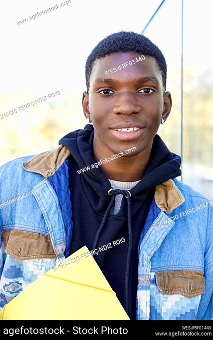 Smiling student with file leaning on wall