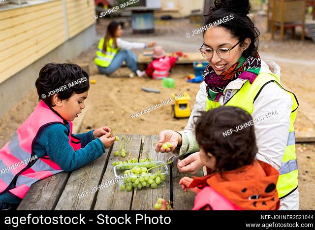 Preschool teacher and students eating grapes outdoors