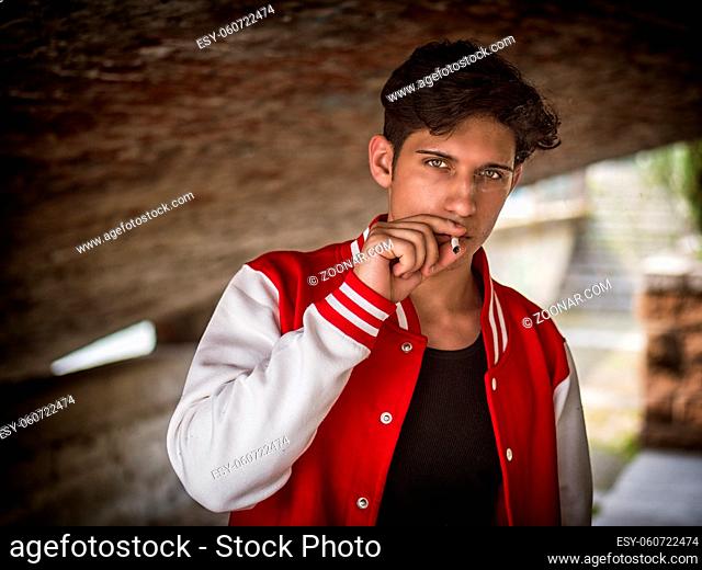 Handsome stylish young man smoking outside in urban setting, looking at camera