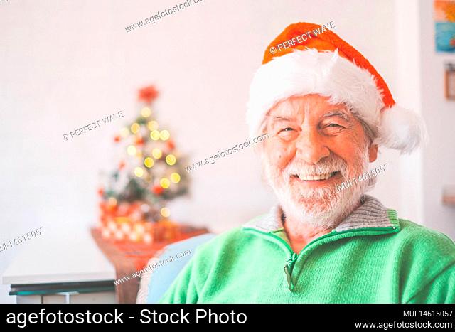 Portrait of smiling retired senior man in santa hat and warm clothing celebrating christmas at home. Old male santa smiling while looking at camera