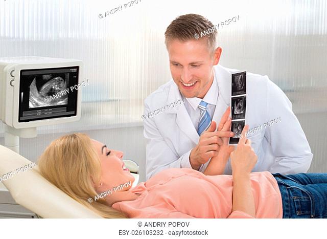 Young male doctor explaining ultrasound scan to pregnant woman in hospital