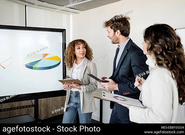 Businesswomen holding clipboards looking at businessman discussing strategy in boardroom