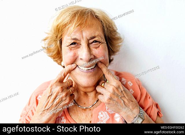 Senior woman holding cheeks in front of white wall