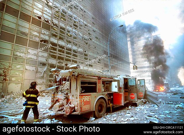 New York City fire fighter pulling water hose from fire truck amid debris and burning buildings following September 11th terrorist attack on World Trade Center
