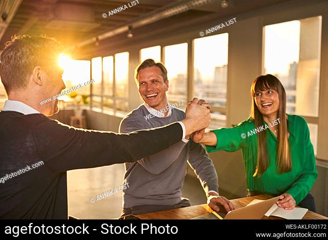Smiling businessman holding hands of colleagues in meeting