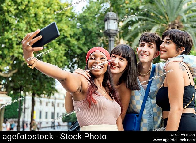 Happy woman with friends taking selfie through mobile phone in park