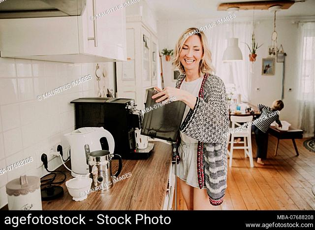 Woman prepares breakfast in the kitchen, son sits at the table in the background