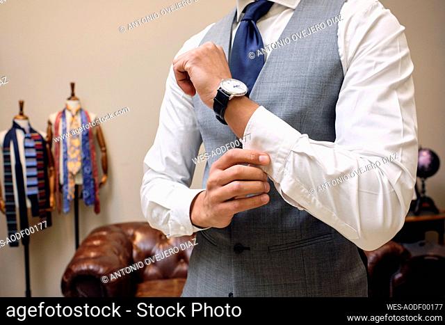 Man in gray waistcoat fastening shirt cuff in tailors boutique
