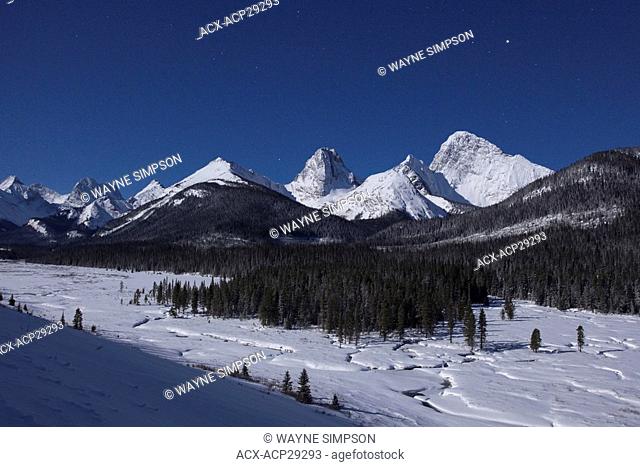 The Rocky Mountains are illuminated by a full moon on a winter night in Spray Valley Provincial Park in Kananaskis Country