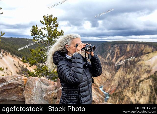 USA, Wyoming, Yellowstone National Park, Senior woman looking through binoculars while standing above Grand Canyon in Yellowstone National Park