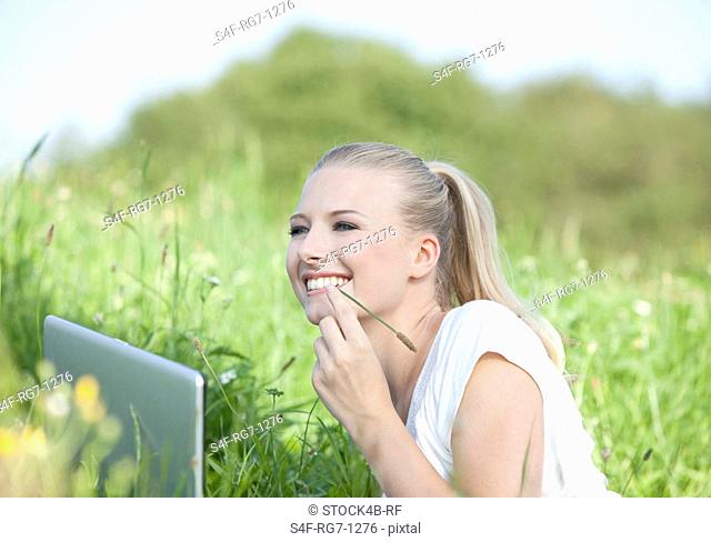 Happy young woman lying in meadow with laptop