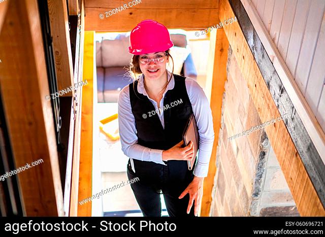 young architect woman smiling on the stairs. Female Civil engineer standing in construction site wearing pink safety hard hat and holding a clipboard