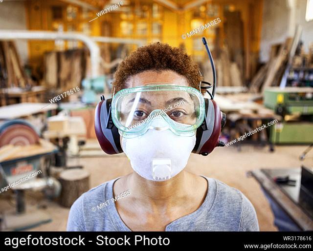 Close up view of black woman factory worker wearing safety glasses and dust nose mask in a woodworking factory