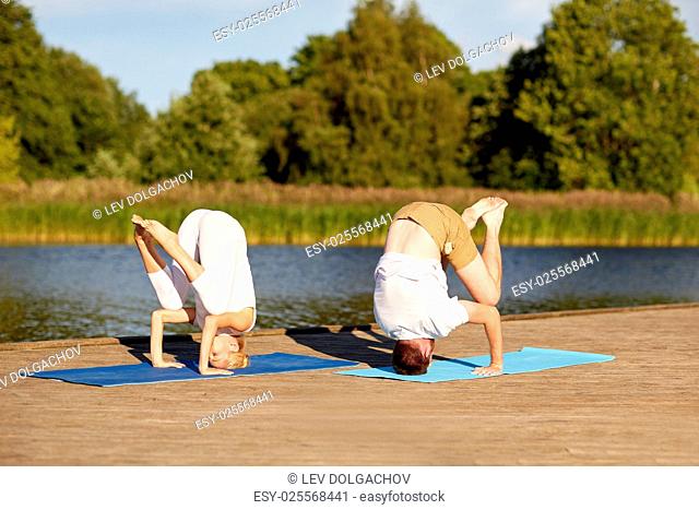 fitness, sport, yoga, people and healthy lifestyle concept - couple making headstand outdoors on river or lake berth