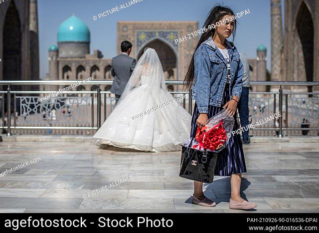26 September 2021, Uzbekistan, Samarkand: An Uzbek woman holds flowers as newlyweds have pictures taken at the historical landmark of Registan in Samarkand