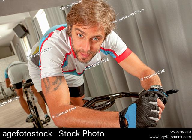 Young handsome and fitt man is looking to camera and posing in a cycling gym